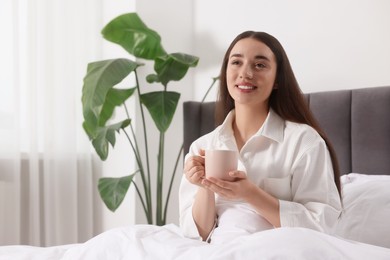Happy woman with cup of drink in bed at home, space for text. Lazy morning