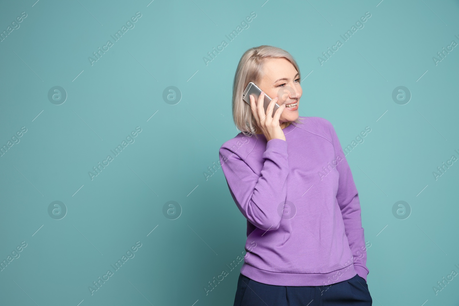 Photo of Mature woman talking on mobile phone against color background