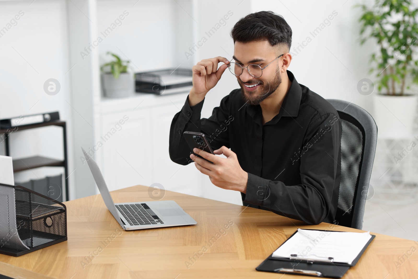 Photo of Handsome young man using smartphone at wooden table in office