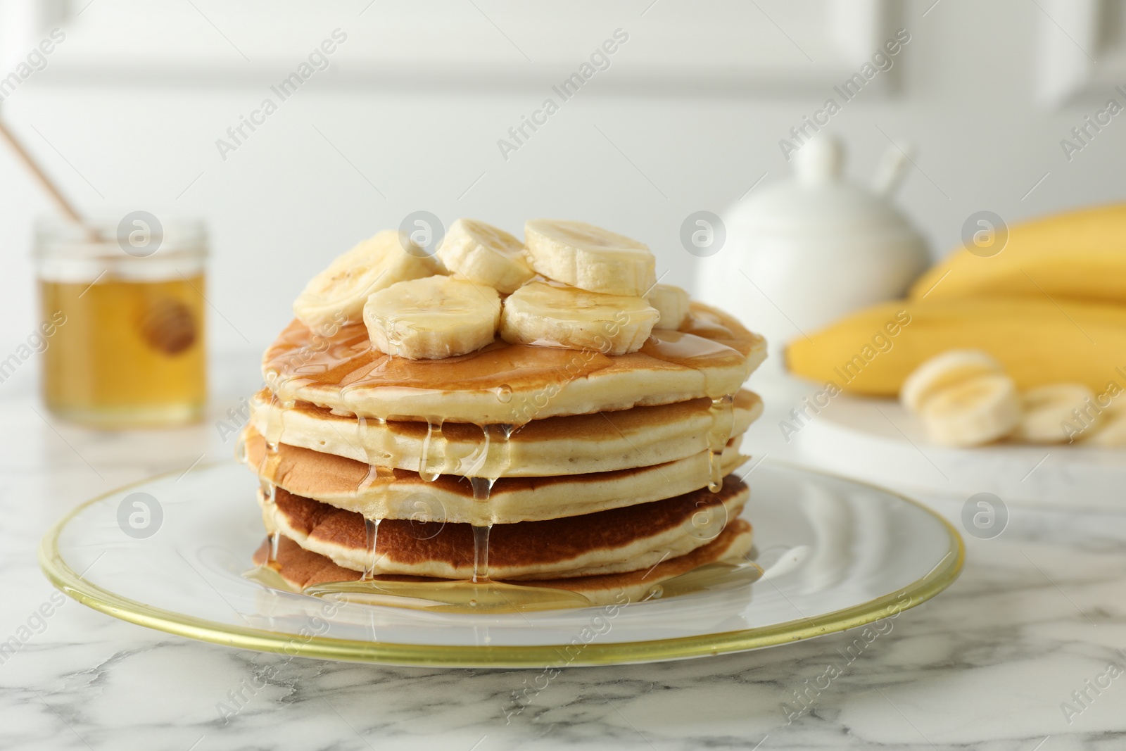 Photo of Delicious pancakes with bananas and honey on white marble table, closeup