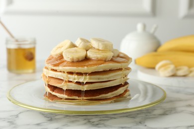 Photo of Delicious pancakes with bananas and honey on white marble table, closeup