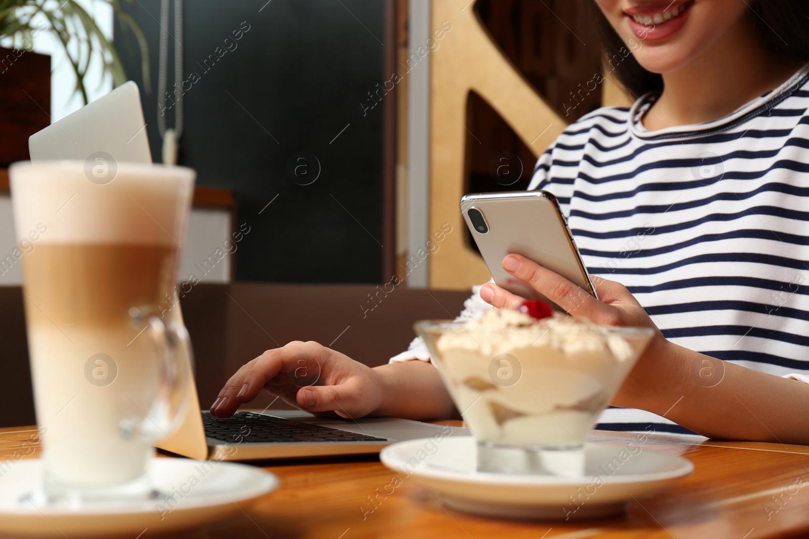 Photo of Young blogger with laptop and smartphone in cafe, closeup