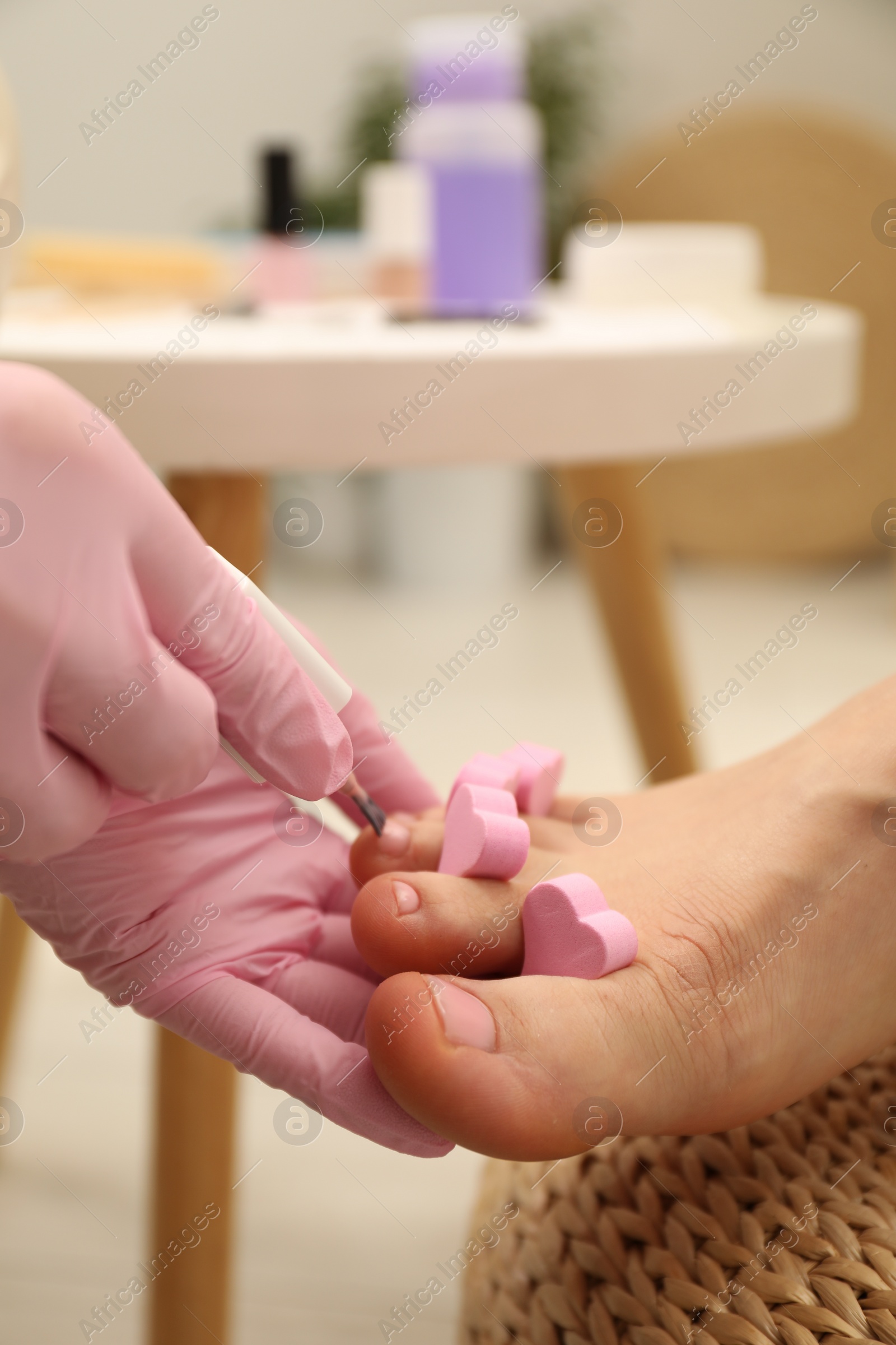 Photo of Professional pedicurist painting client`s toenails with polish in beauty salon, closeup