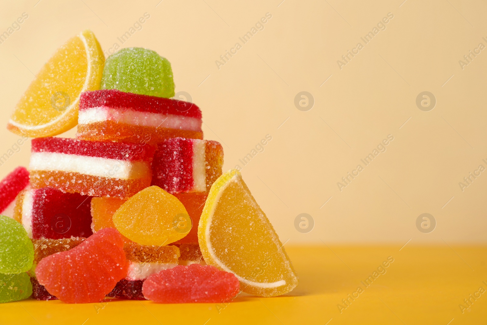 Photo of Pile of delicious bright jelly candies on yellow table. Space for text