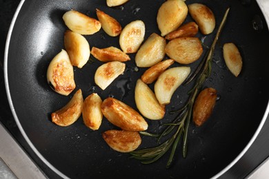 Photo of Frying pan with fried garlic cloves and rosemary, top view