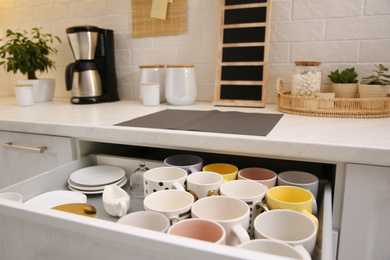 Photo of Open drawer with cups and coffeemaker on countertop in kitchen