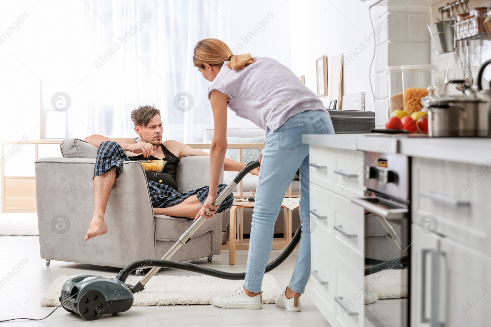 Photo of Lazy husband watching TV and his wife cleaning at home