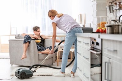 Photo of Lazy husband watching TV and his wife cleaning at home