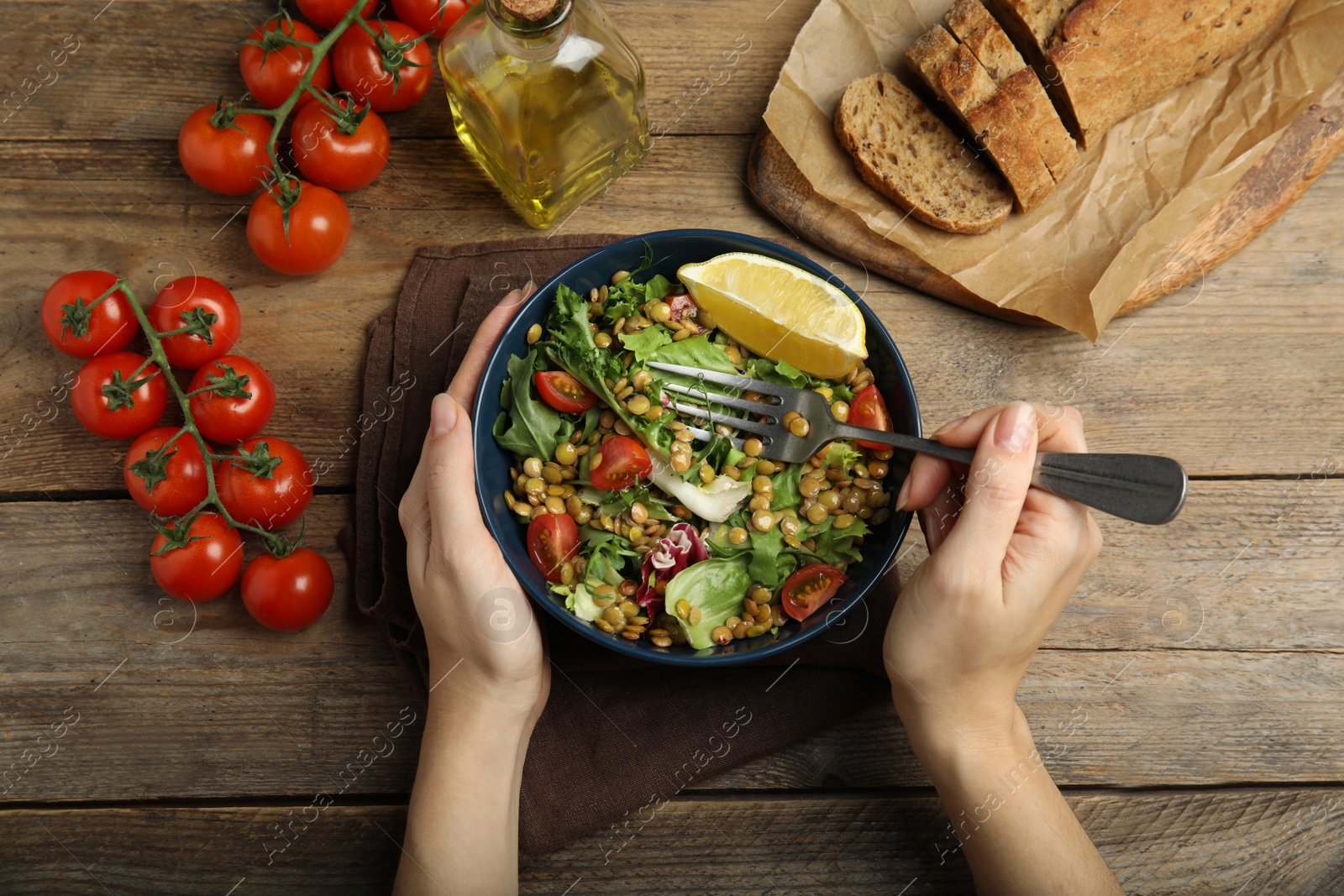 Photo of Woman eating delicious salad with lentils and vegetables at wooden table, top view