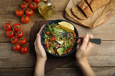 Photo of Woman eating delicious salad with lentils and vegetables at wooden table, top view