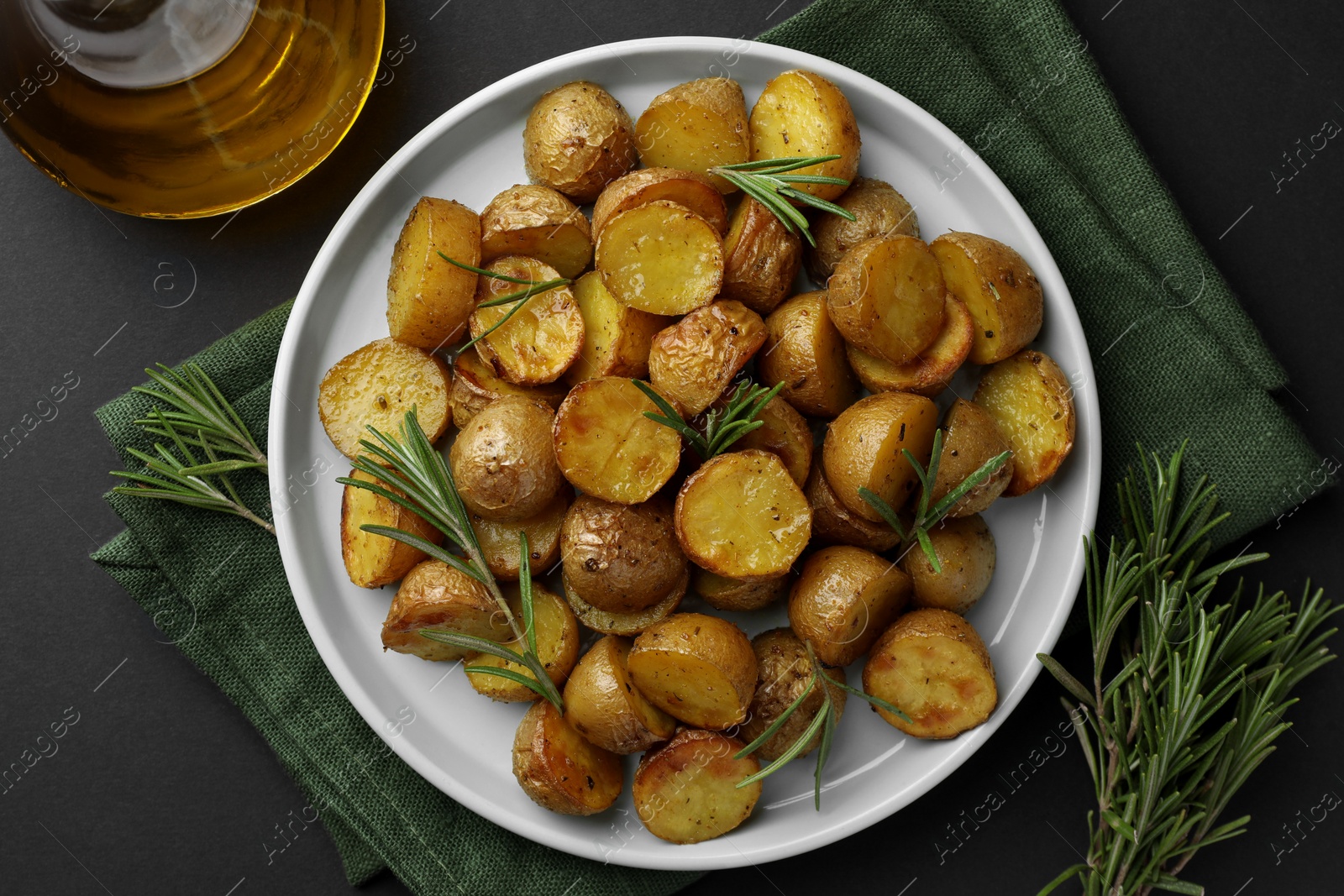 Photo of Delicious baked potatoes with rosemary and oil on black table, top view