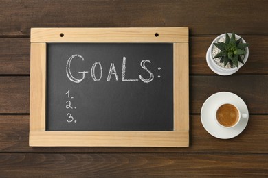 Photo of Small blackboard with empty list of goals, houseplant and cup of coffee on wooden table, flat lay. Space for text