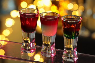 Photo of Different shooters in shot glasses on surface against blurred background, closeup Alcohol drink