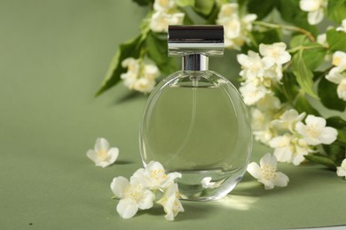 Photo of Aromatic perfume in bottle among beautiful jasmine flowers on pale green background