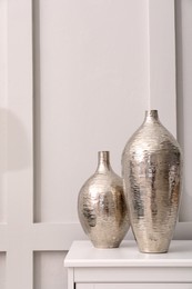 Shiny vases on white table indoors. Interior element