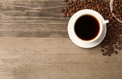 Cup of aromatic coffee and beans on wooden table, flat lay. Space for text