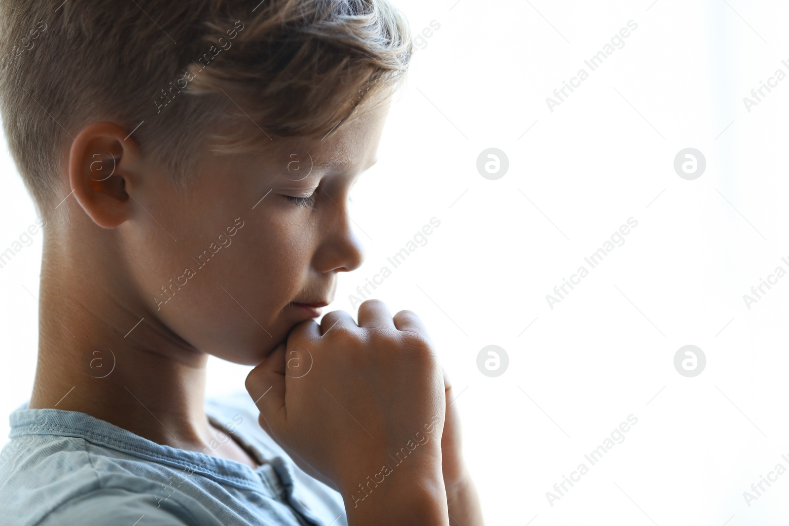 Photo of Little boy with hands clasped together for prayer on light background. Space for text