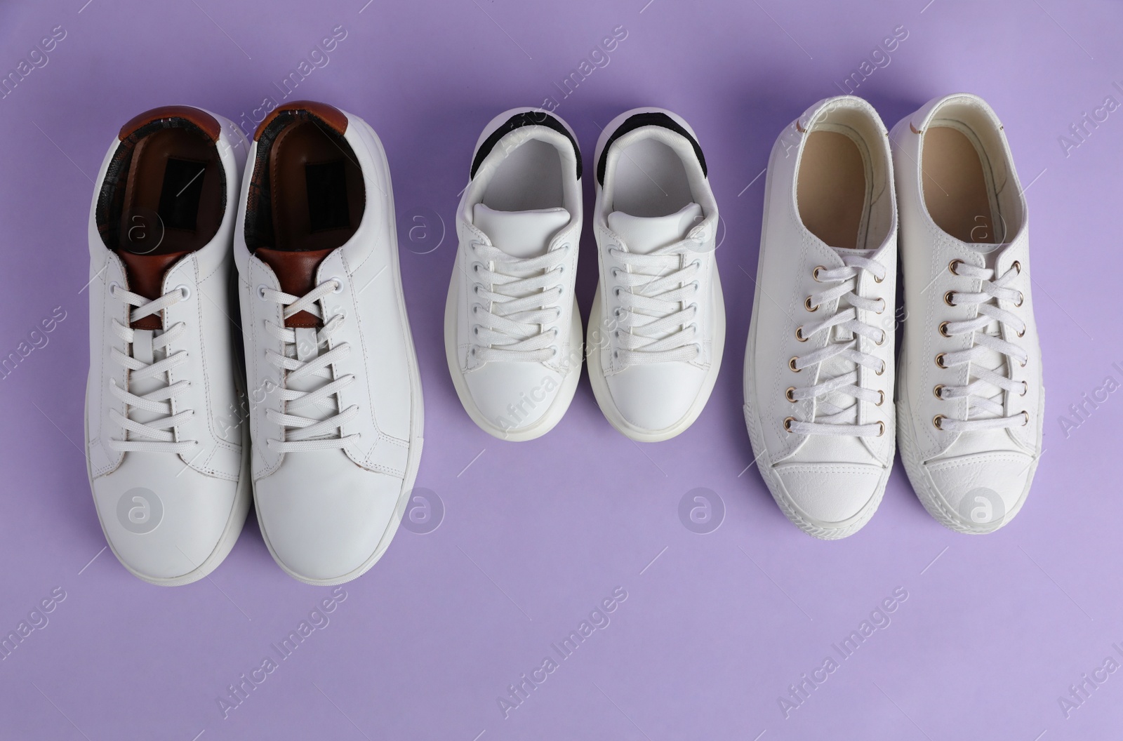 Photo of Set of new stylish white sneakers for entire family on violet background, flat lay