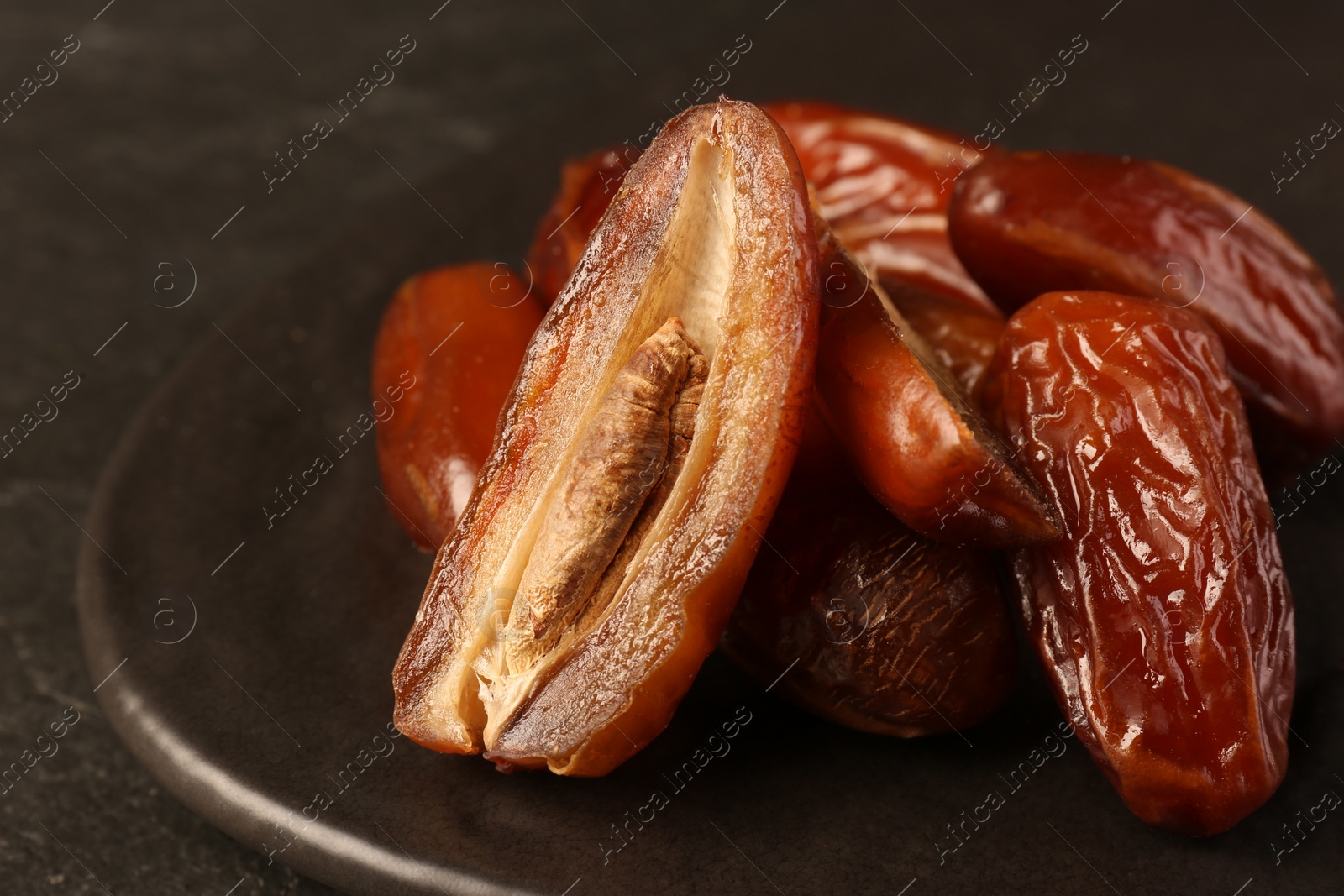 Photo of Whole and cut tasty sweet dried dates on black table, closeup