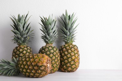 Whole ripe pineapples on white wooden table, space for text