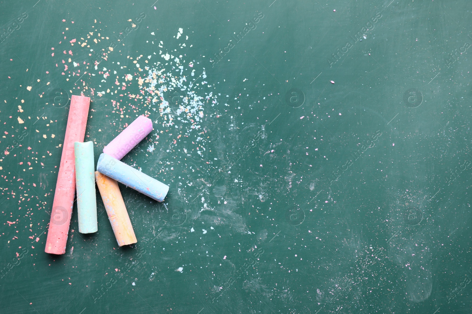 Photo of Pieces of color chalk on greenboard, flat lay. Space for text