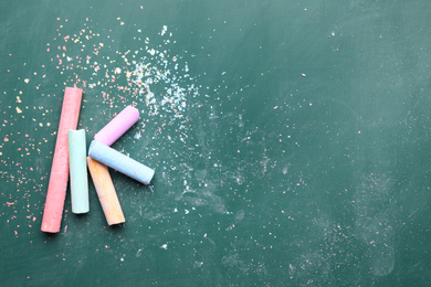 Photo of Pieces of color chalk on greenboard, flat lay. Space for text