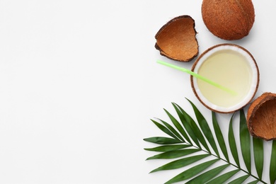 Composition with drink in half of coconut and palm leaf on white background, top view