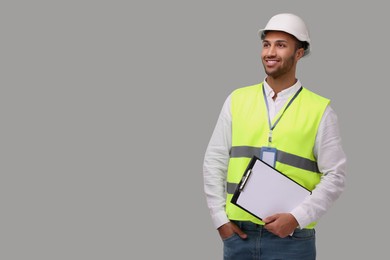 Photo of Engineer in hard hat holding clipboard on grey background, space for text