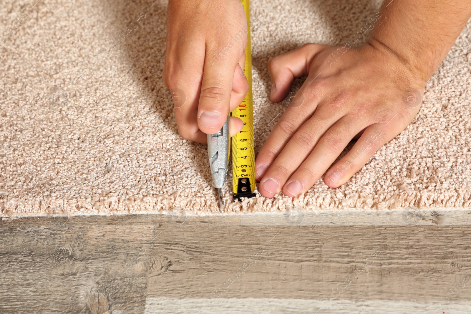 Photo of Man cutting new carpet flooring indoors, closeup