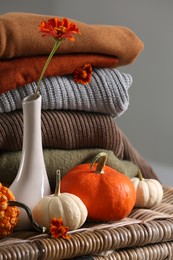 Beautiful autumn flowers, pumpkins and stacked clothes on wicker table