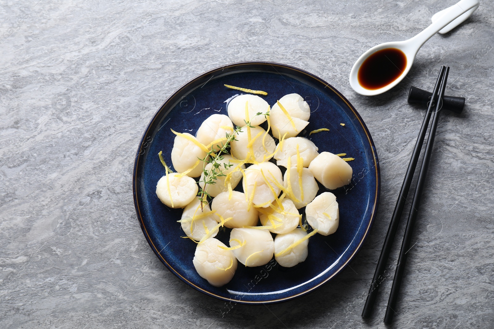 Photo of Raw scallops with thyme and lemon zest served on grey marble table, flat lay. Space for text