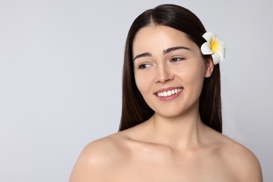 Photo of Young woman with plumeria flower in hair on light grey background, space for text. Spa treatment
