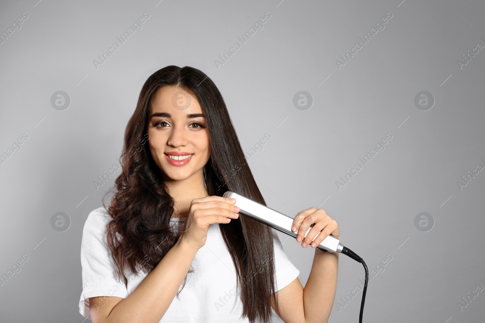 Photo of Happy woman using hair iron on grey background. Space for text