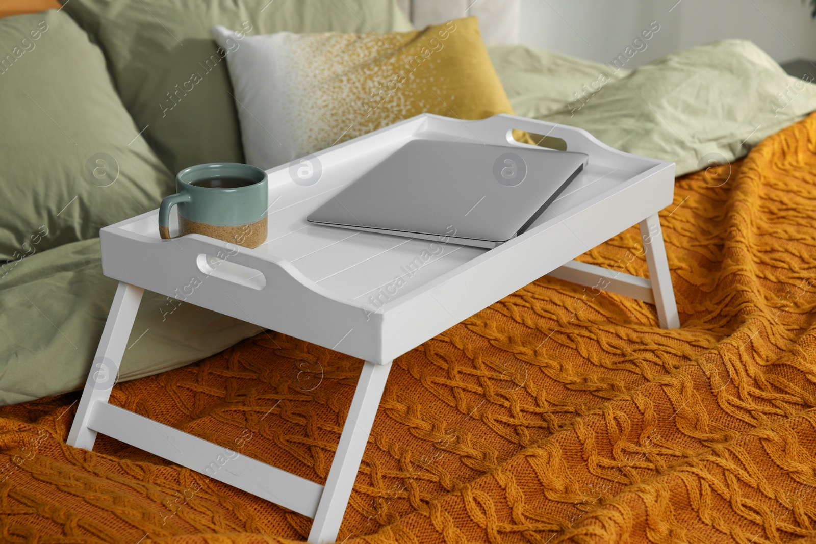 Photo of White tray with modern laptop and cup of aromatic tea on bed indoors