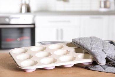 Photo of Clean baking dish, muffin pan and oven glove on table in kitchen. Space for text