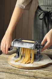 Photo of Woman making homemade noodles with pasta maker at wooden table, closeup