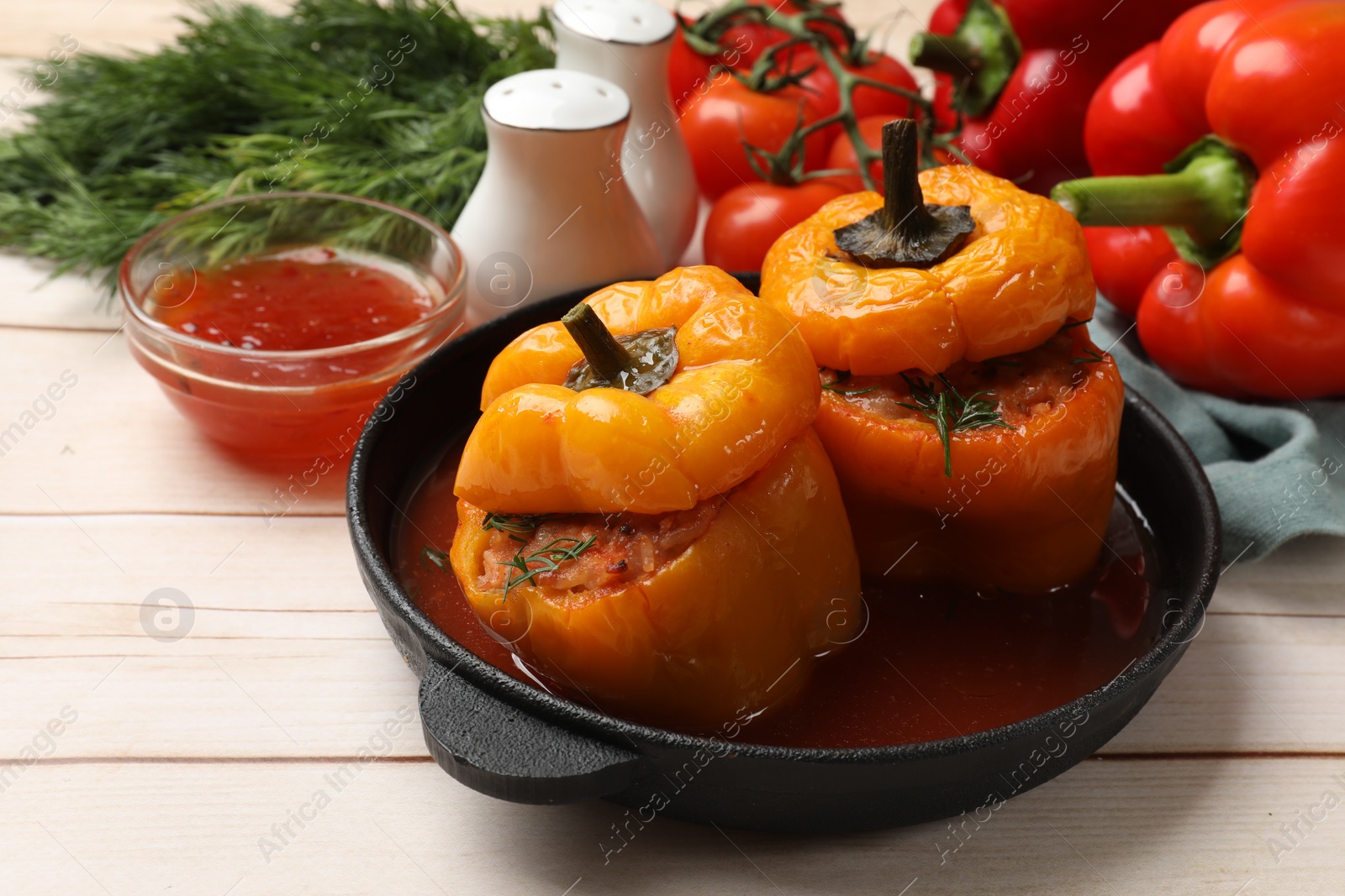 Photo of Tasty stuffed peppers in pan, sauce and products on light wooden table, closeup