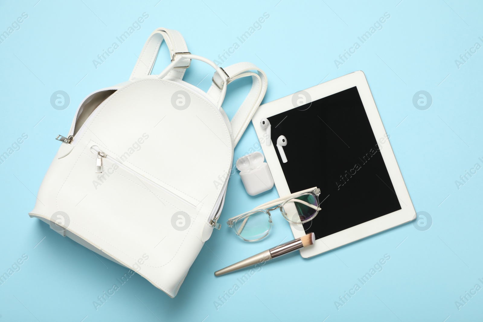 Photo of Stylish urban backpack with different items on light blue background, flat lay