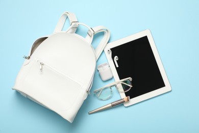 Photo of Stylish urban backpack with different items on light blue background, flat lay