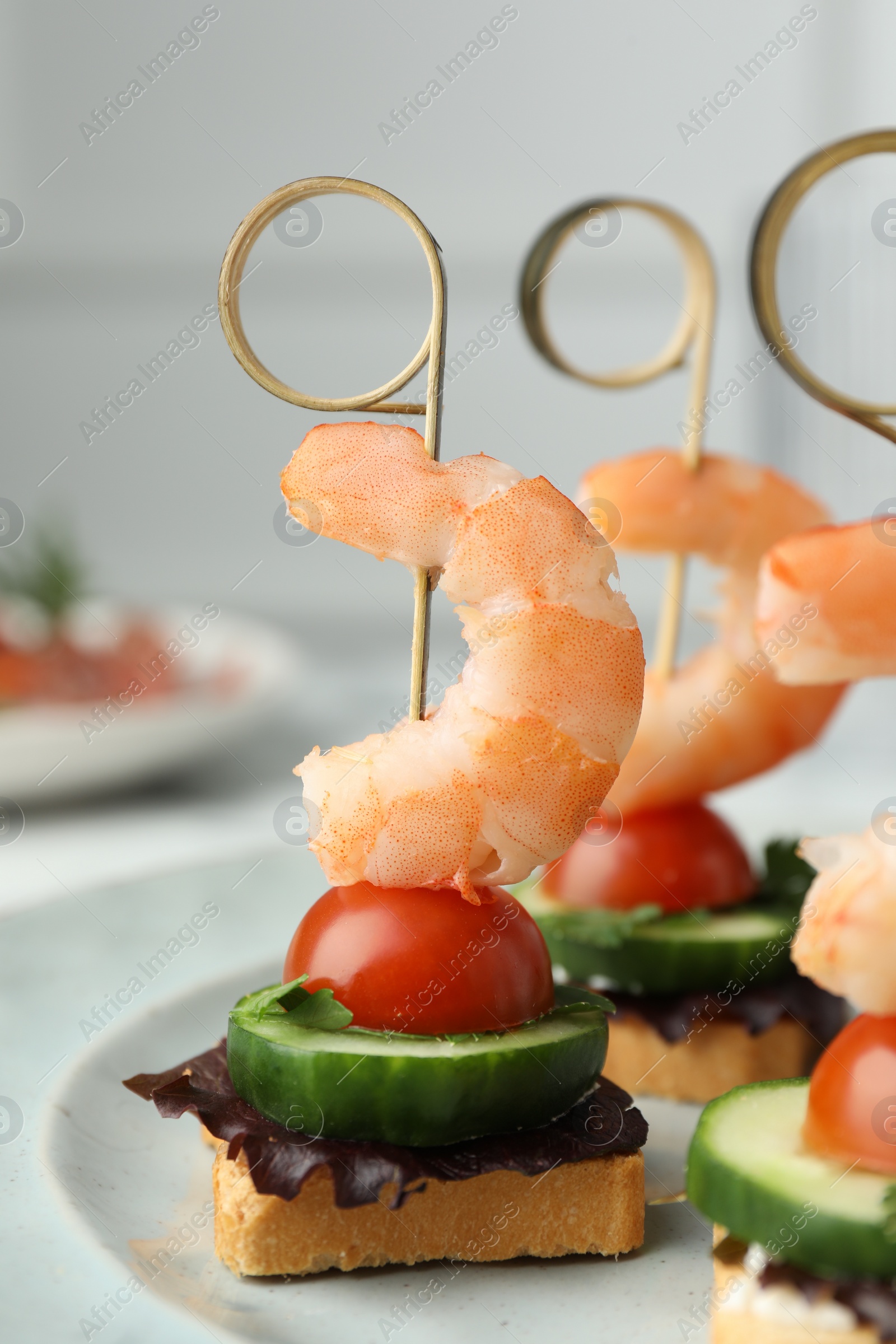 Photo of Tasty canapes with shrimps, cucumber, greens and tomatoes on plate, closeup