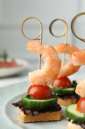 Photo of Tasty canapes with shrimps, cucumber, greens and tomatoes on plate, closeup