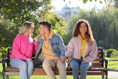 Man flirting with another woman while holding girlfriend's hand on bench in park. Love triangle