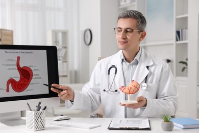 Photo of Gastroenterologist with human model showing screen with illustration of stomach at table in clinic