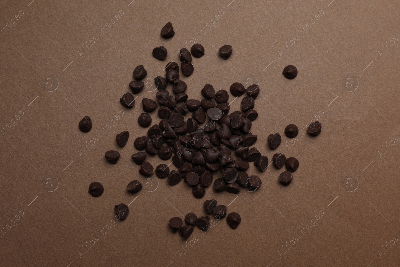 Photo of Pile of delicious chocolate chips on brown background, top view