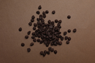 Photo of Pile of delicious chocolate chips on brown background, top view