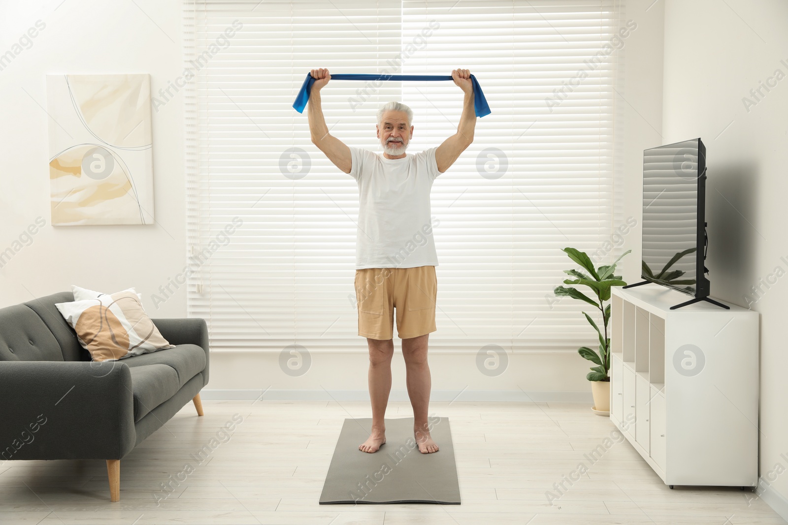 Photo of Senior man doing exercise with fitness elastic band on mat at home