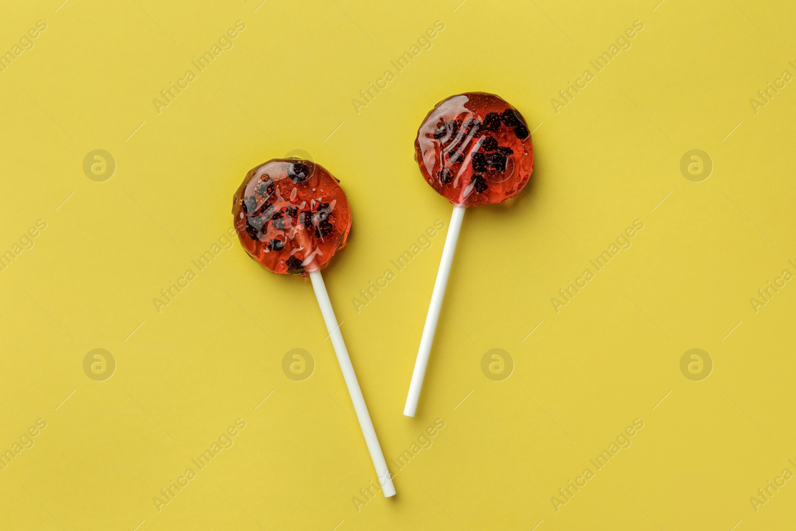 Photo of Sweet colorful lollipops with berries on yellow background, flat lay
