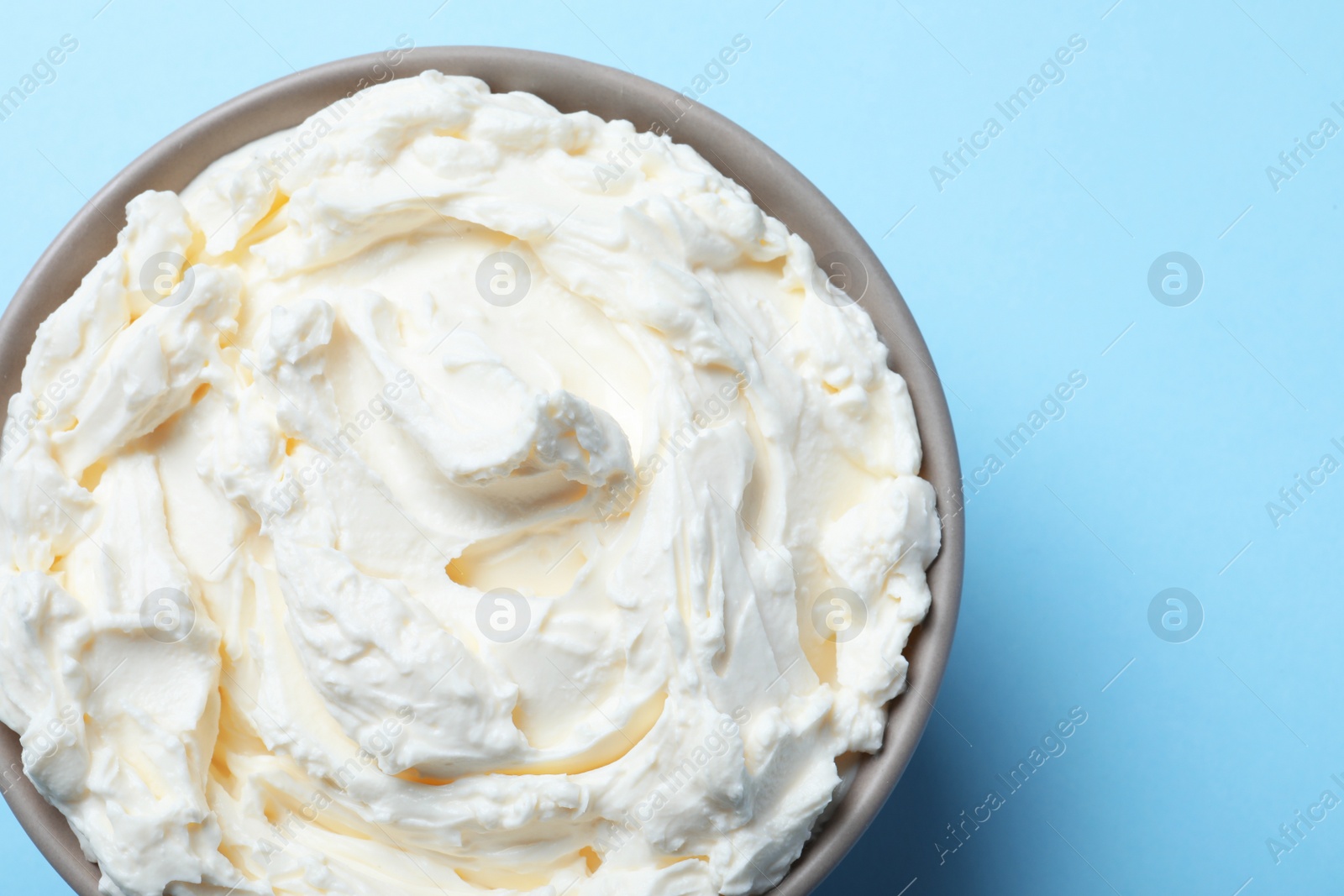 Photo of Bowl of tasty cream cheese on light blue background, top view