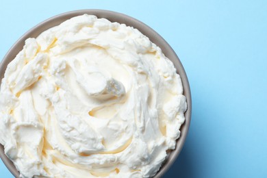 Photo of Bowl of tasty cream cheese on light blue background, top view