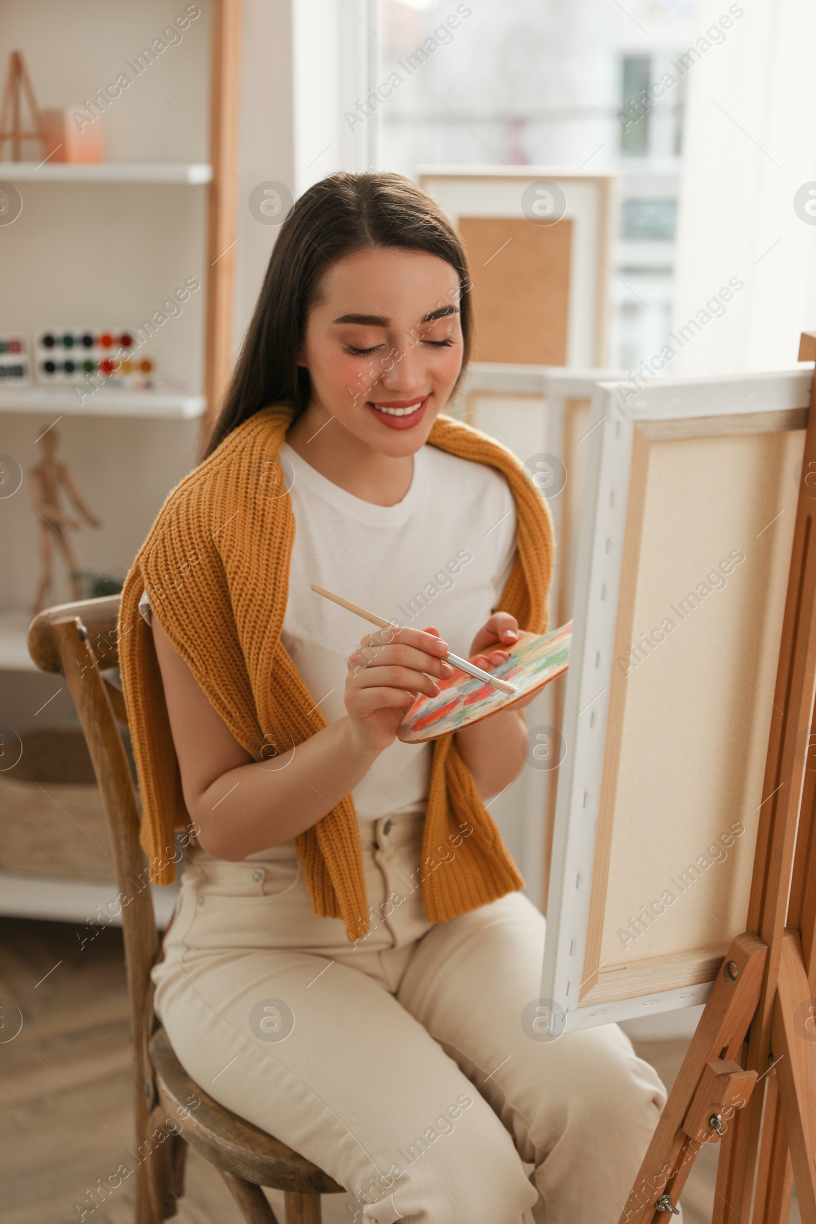 Photo of Beautiful young woman drawing on easel at home